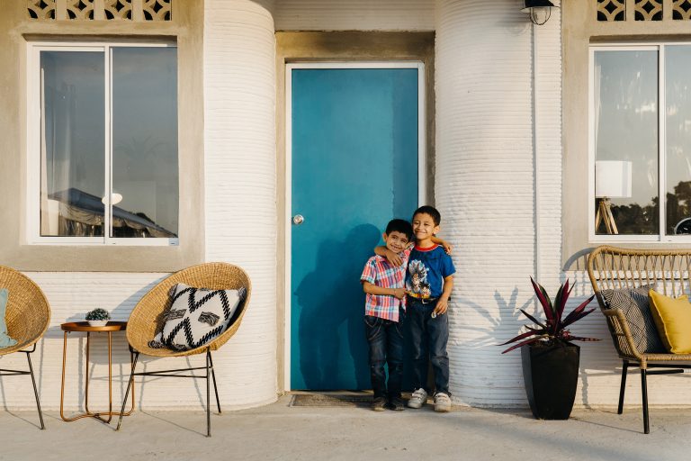 Two young brothers in front of their 3d-printed home