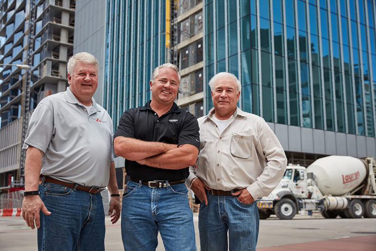 3 men standing in front of building and concrete mixer truck