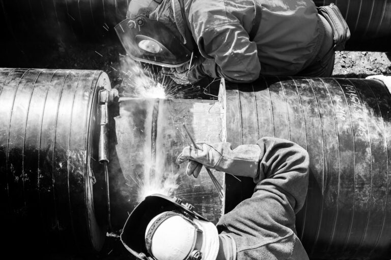 two skilled workers welding together a pipe